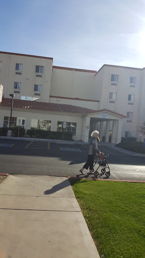 A senior person walking with a walker in front of a hotel on a sunny day.