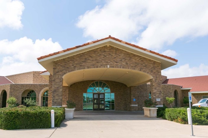 A building entrance with a stone facade and arched design under a partly cloudy sky.