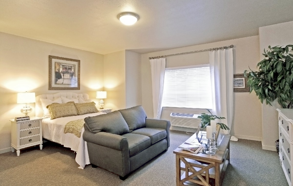 A cozy bedroom featuring a bed, a sofa, and a window with curtains.