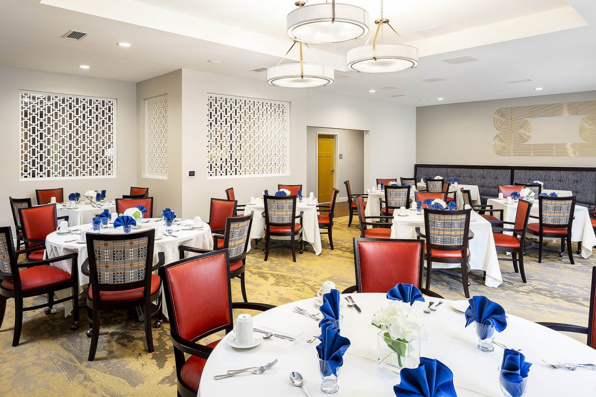 A well-appointed dining room with elegantly set tables featuring blue napkins and comfortable red chairs.
