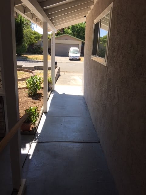 A shaded walkway leading to a sunny driveway with a car parked in front of a garage.