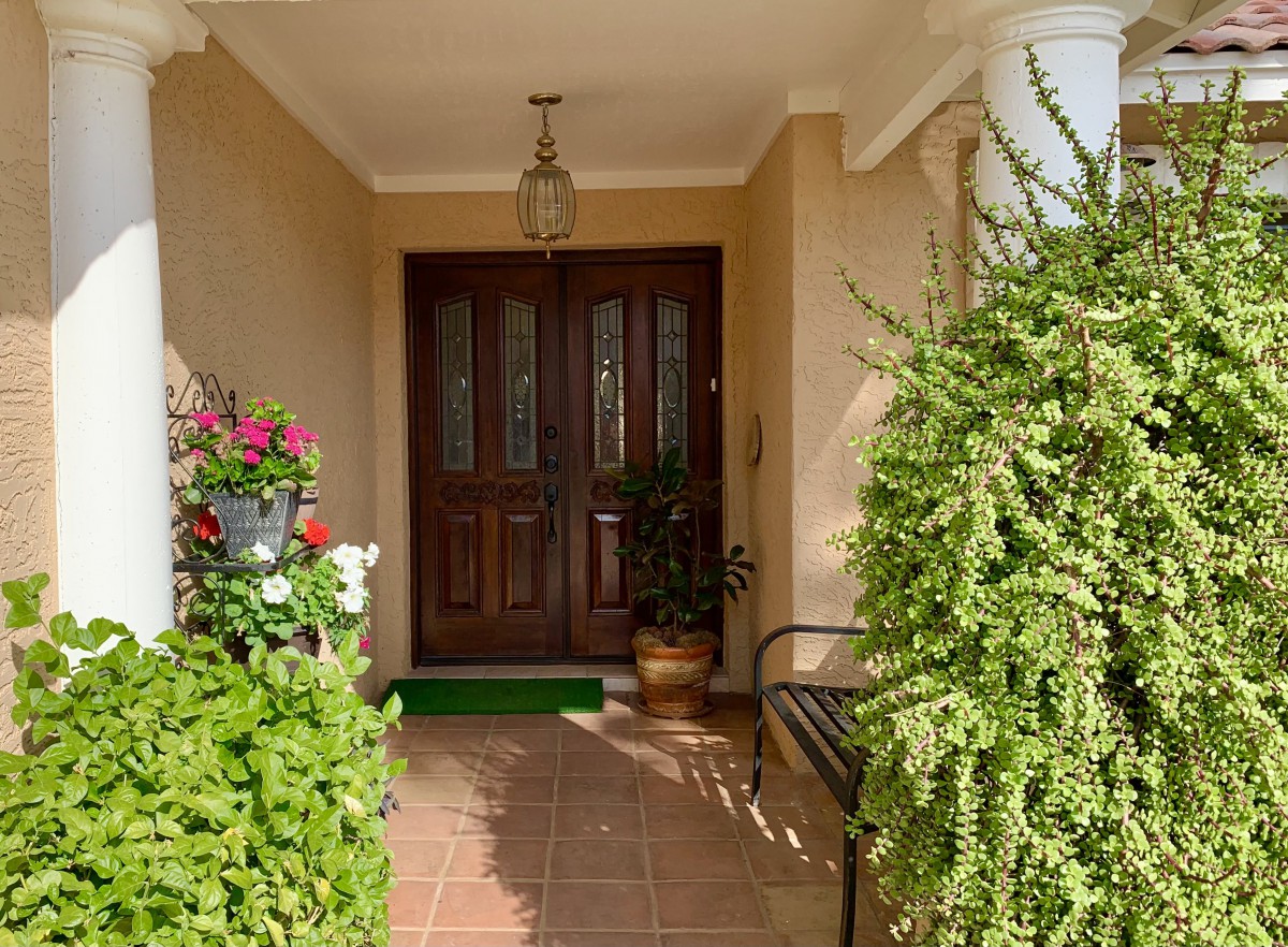 A welcoming front porch with a wooden door, adorned by lush plants and vibrant flowers.