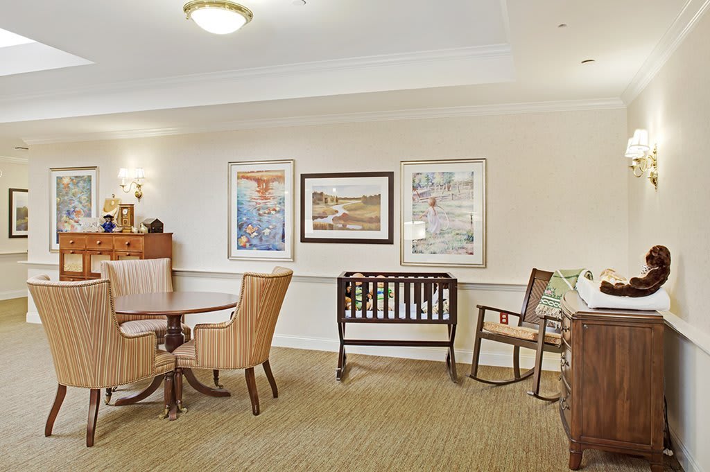 A cozy living room with comfortable chairs, a table, and various artworks on the wall.