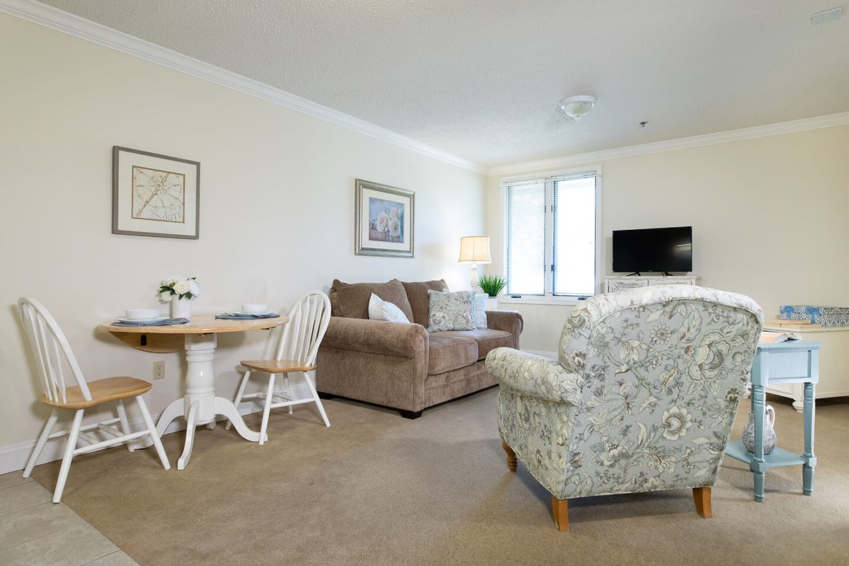 A cozy living room with a sofa, armchair, dining table, and television.
