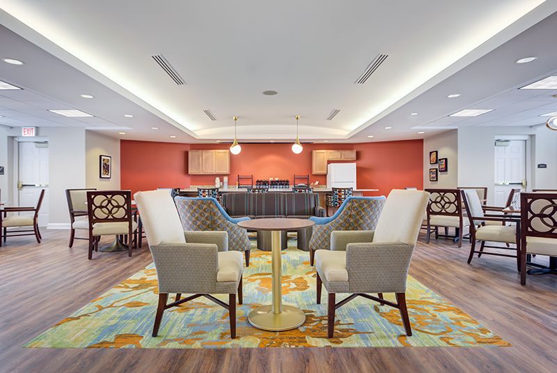 A stylish lounge area with comfortable chairs and a central table, accented by warm lighting and colorful carpeting.