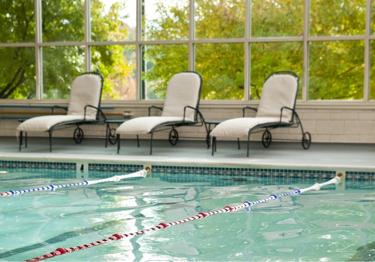 A serene indoor pool area with three lounge chairs by the side.