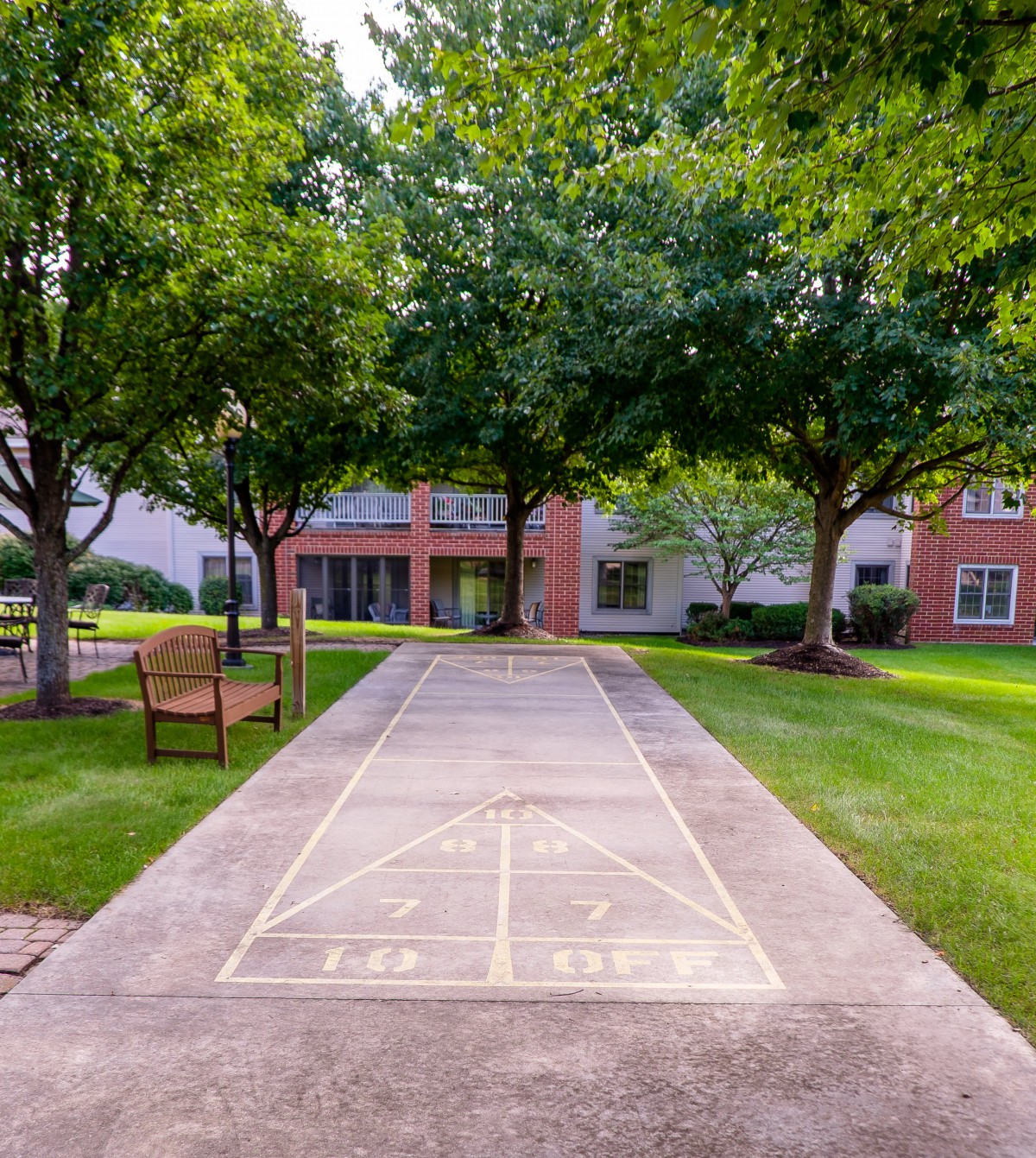 A scenic courtyard with a shuffleboard court, surrounded by trees and a bench.