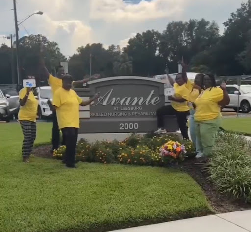 A joyful group in yellow shirts celebrating by a community sign.