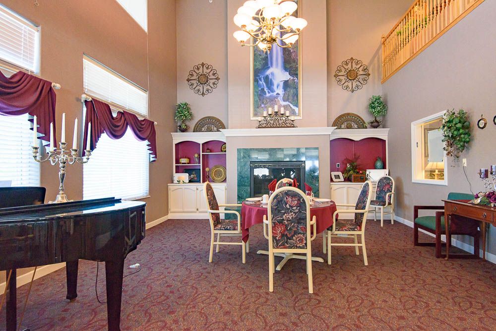 A luxurious living room with a high ceiling, featuring a fireplace, dining table, chairs, and a piano.