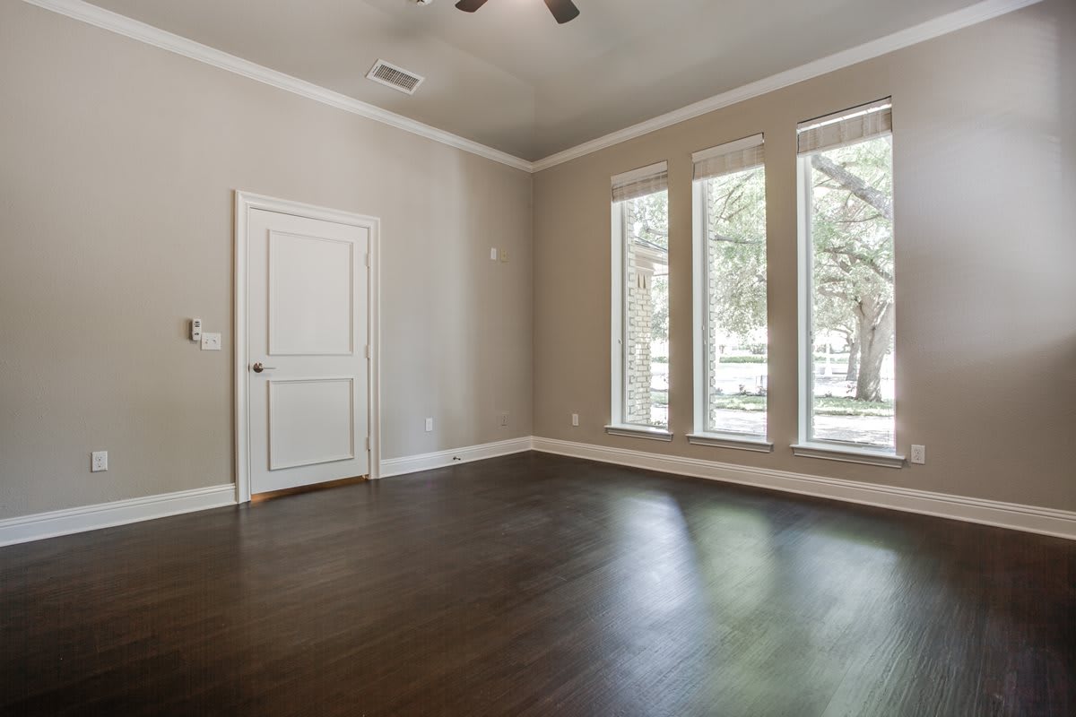 An empty room with hardwood flooring and large windows allowing natural light to enter.