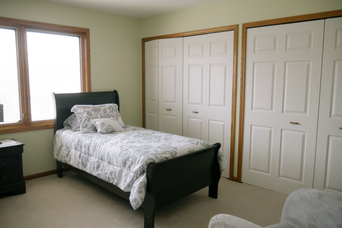 A simple bedroom featuring a single bed, closet doors, and a window.