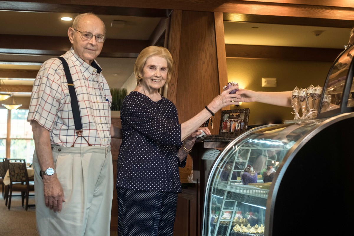 An elderly couple is at a coffee shop, completing a transaction for desserts.