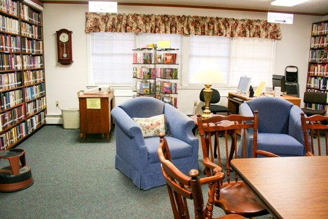 A cozy library interior with blue chairs, a bookshelf, and a clock on the wall.