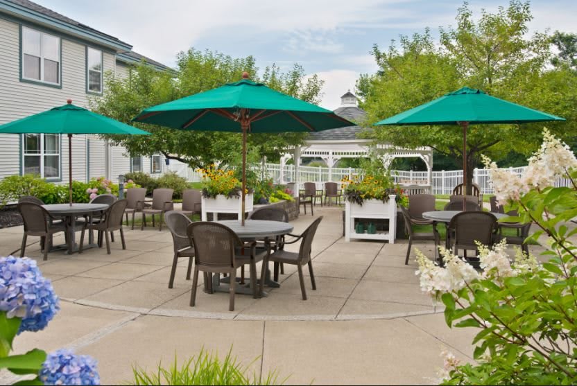 A spacious outdoor patio with tables, chairs, and green umbrellas surrounded by greenery and a gazebo in the background.