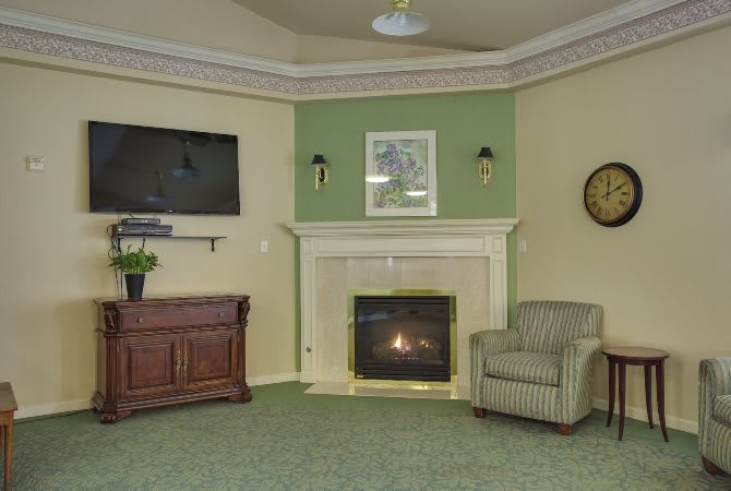 A cozy living room with a fireplace, television, and armchair accented by green walls and a carpeted floor.