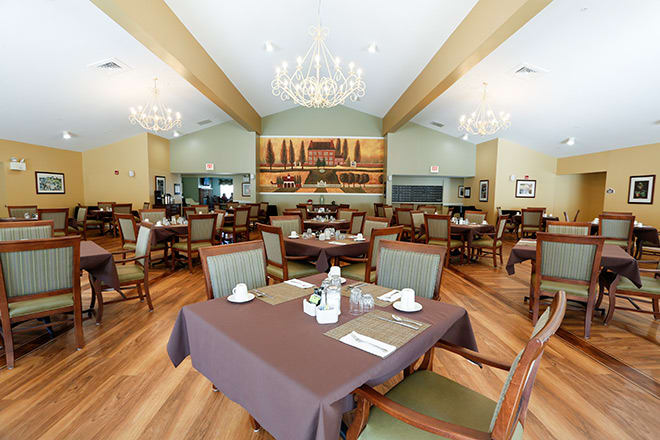 A spacious and elegantly decorated dining area with neatly arranged tables and chairs, illuminated by chandeliers.