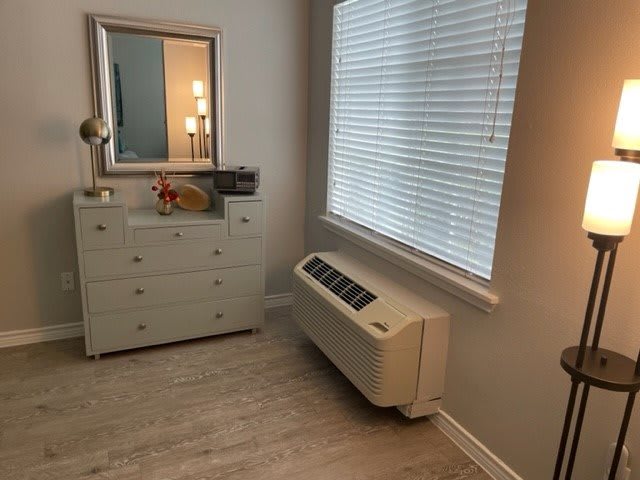 A cozy bedroom corner featuring a dresser with a mirror, a window with blinds, and an air conditioning unit.