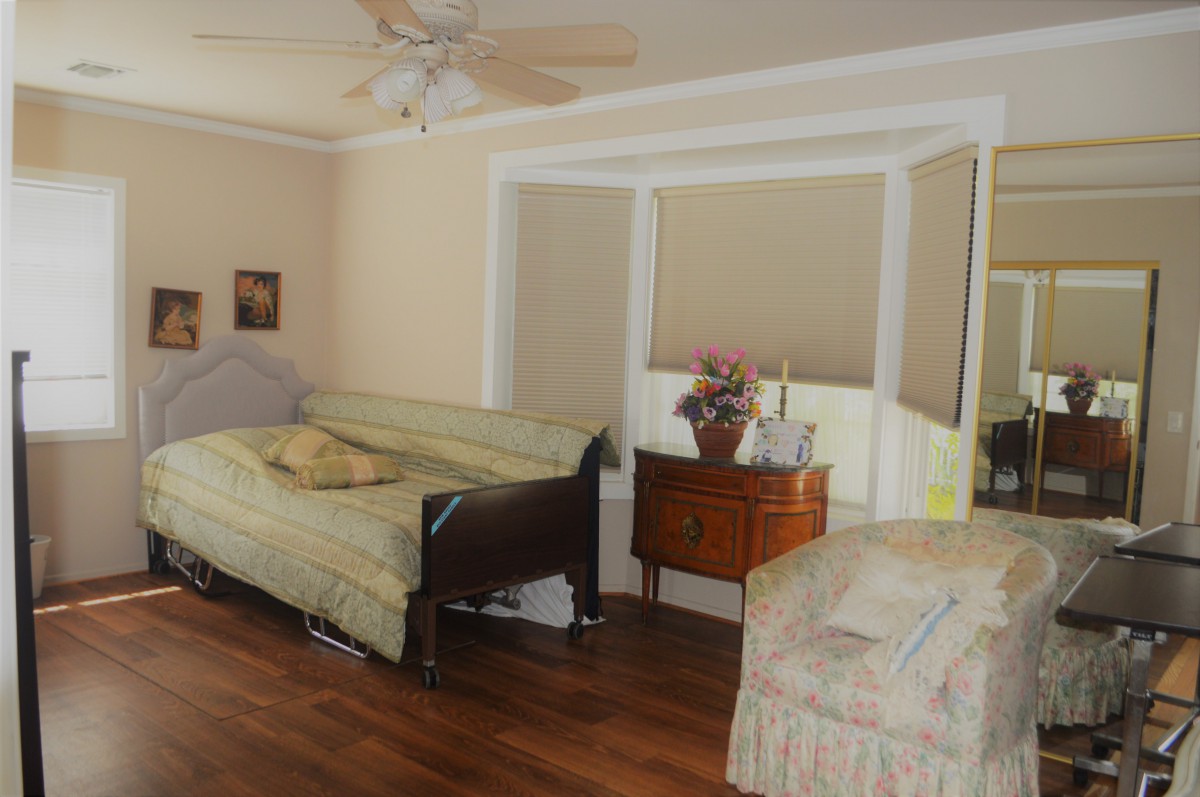 A cozy bedroom with a hospital bed, wooden floors, and large windows.