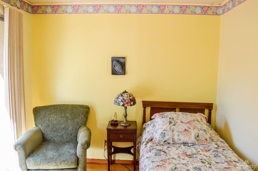 A cozy bedroom with a floral bedspread, vintage lamp, and comfortable chair.