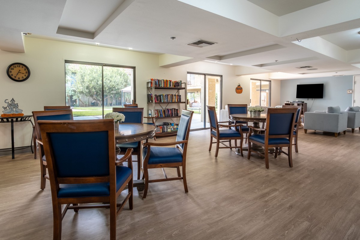A cozy reading area with tables, chairs, and bookshelves illuminated by natural light through large windows.