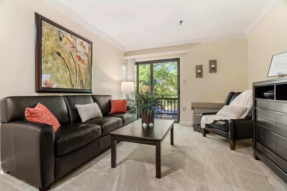 A modern living room featuring a black sofa, coffee table, and colorful artwork, with ample natural light from the sliding door.