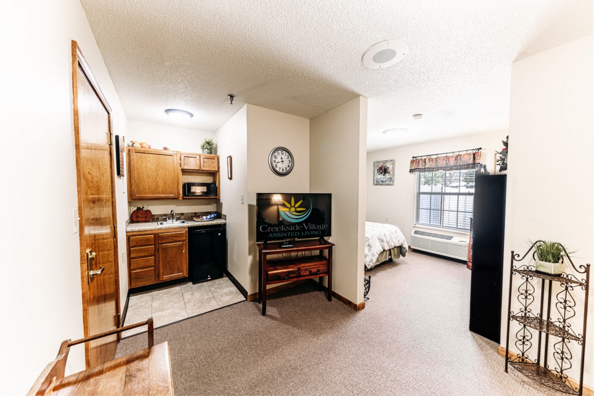 A cozy studio apartment featuring a kitchenette and a small living area with a television.
