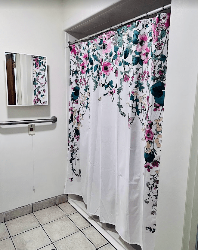 A bathroom with a floral shower curtain and a mirror on the wall.