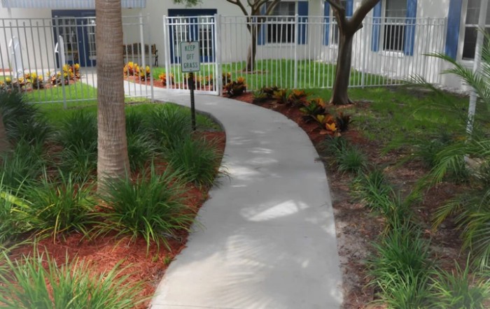A curved pathway through a landscaped garden with trees and plants, bordered by a white fence.