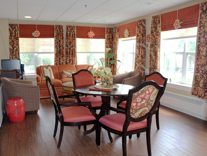 A cozy living room with a round table and four upholstered chairs, surrounded by sofas and adorned with patterned curtains.