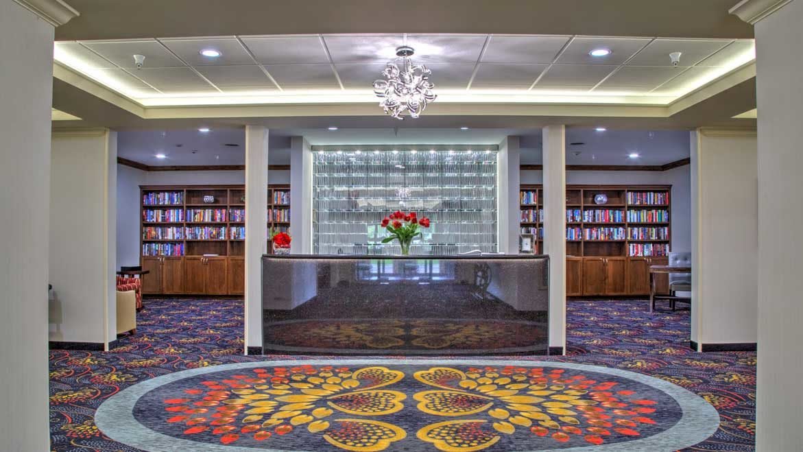 A modern lobby with a reception desk, surrounded by bookshelves and decorated with a colorful carpet.