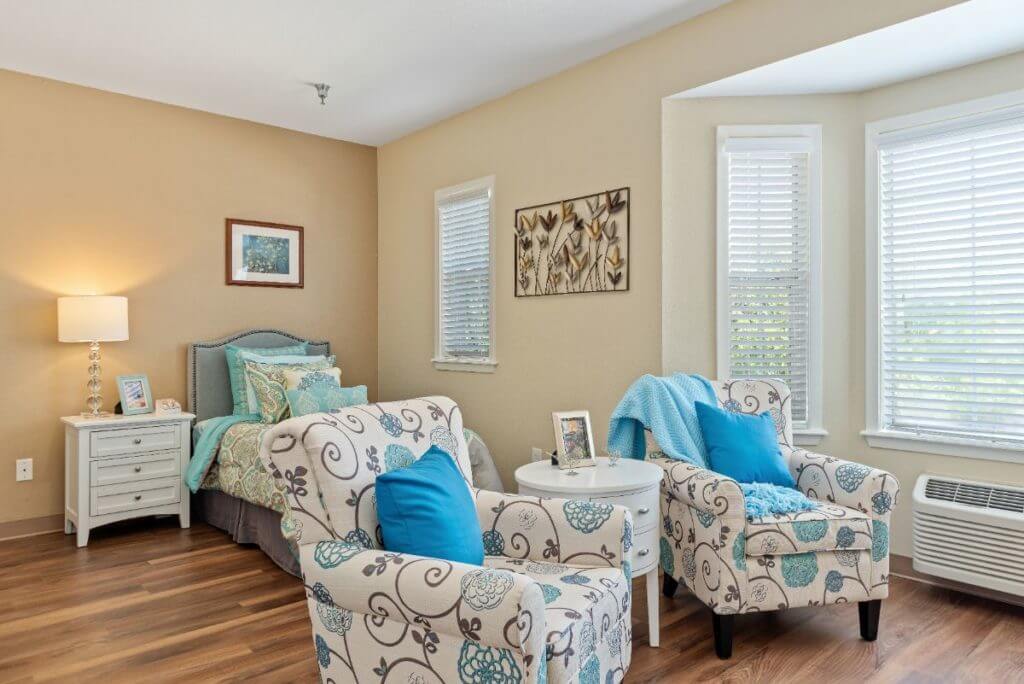 A cozy bedroom with stylish decor, featuring a bed with blue accents, patterned chairs, and framed artwork on the walls.