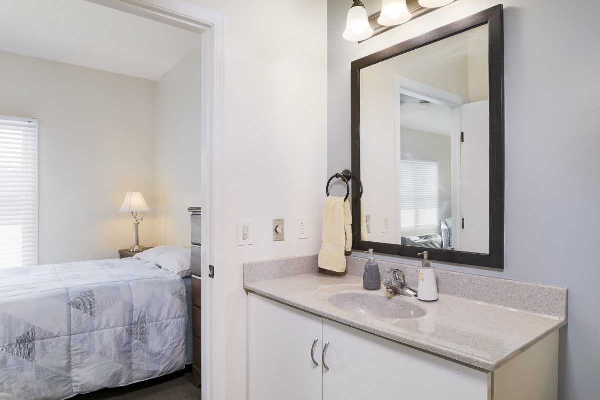 A bathroom with a sink and mirror adjacent to a bedroom.