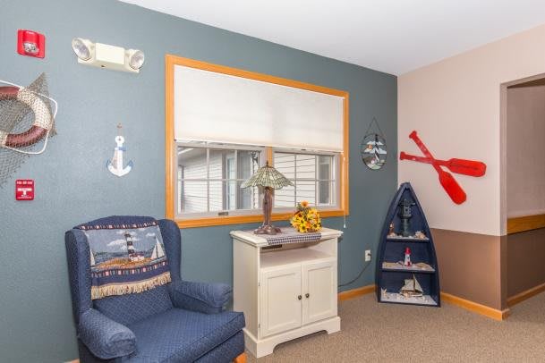 A cozy living room with nautical-themed decor, featuring a blue armchair, decorative sailboat, and anchor embellishments.
