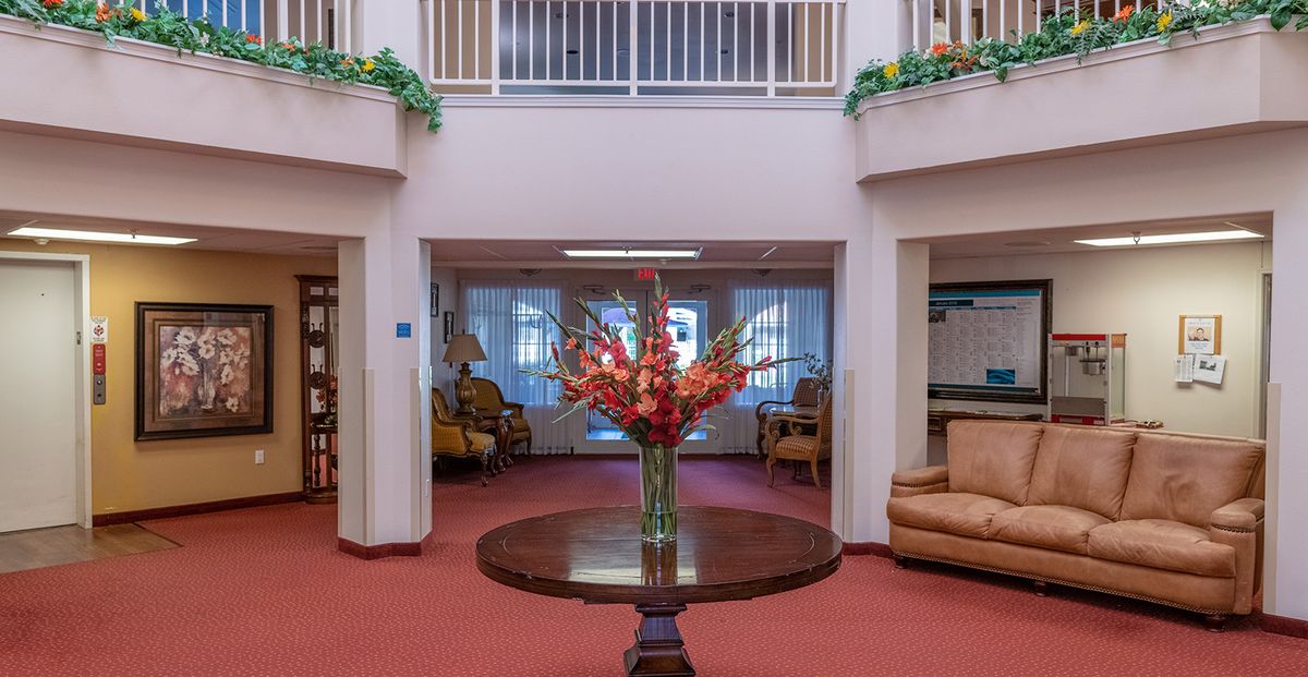 A spacious lobby with a central flower arrangement on a wooden table, surrounded by comfortable seating.