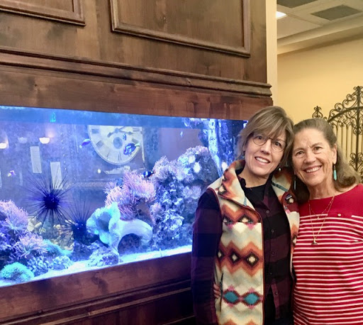Two friends enjoying a moment in front of a vibrant aquarium.