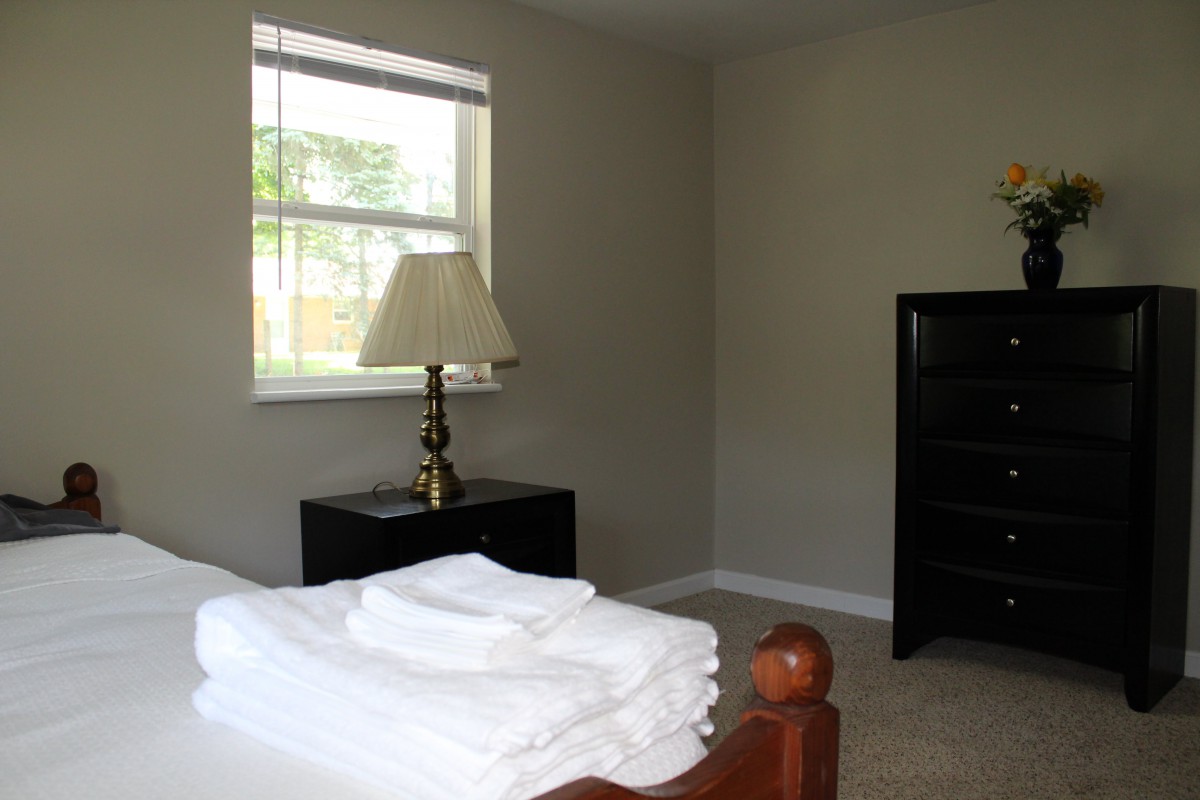 A minimalist bedroom with a window, lamp, and neatly folded linens on the bed.
