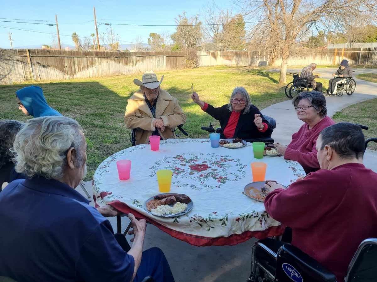 A group of elderly people enjoying an outdoor gathering around a table with food and drinks.