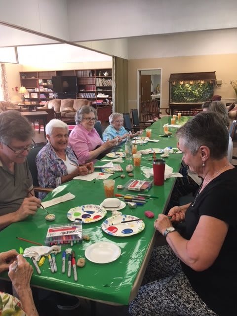 A group of seniors participates in a painting and craft activity around a large table.