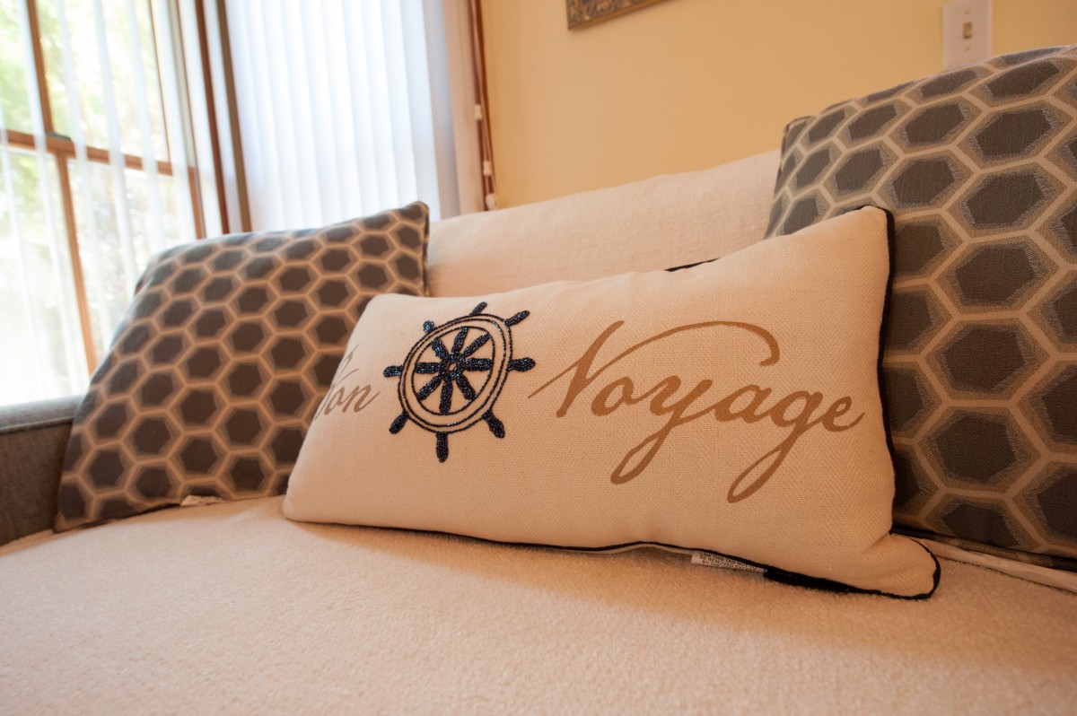 A cozy living room setting featuring a nautical-themed decorative pillow with the word 'Voyage' embroidered on it.