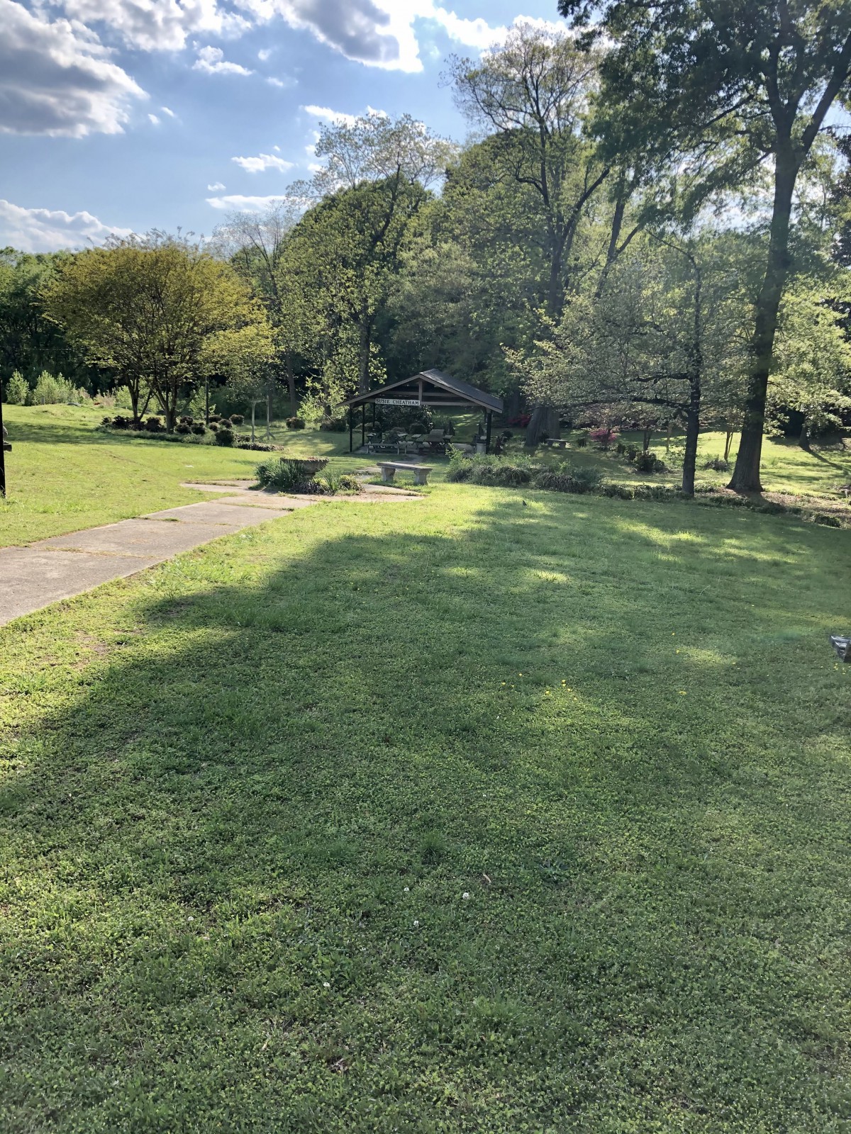 A serene garden landscape with a grassy area, trees, and a pathway on a sunny day.