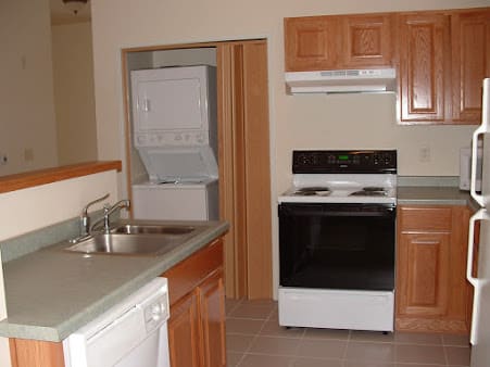 A kitchen with wooden cabinets, a stove, and a stacked washer and dryer set.