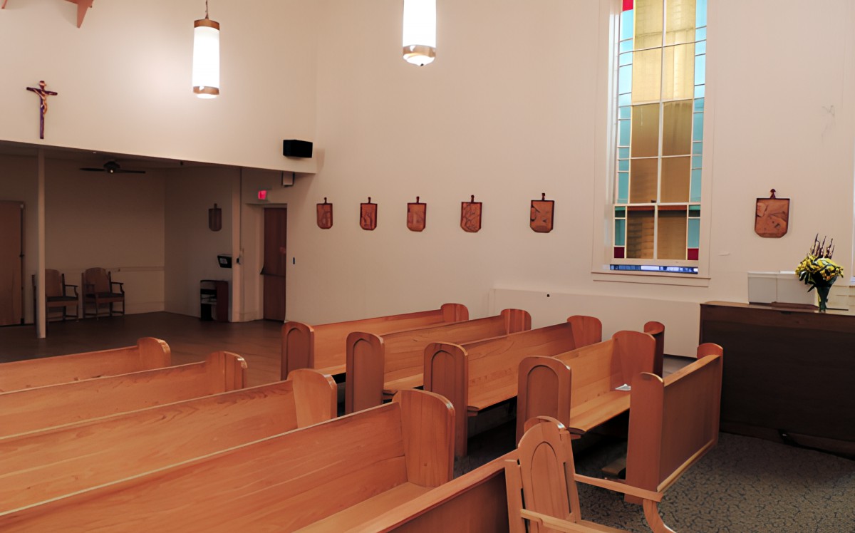 Interior of a church with wooden pews and a stained glass window.