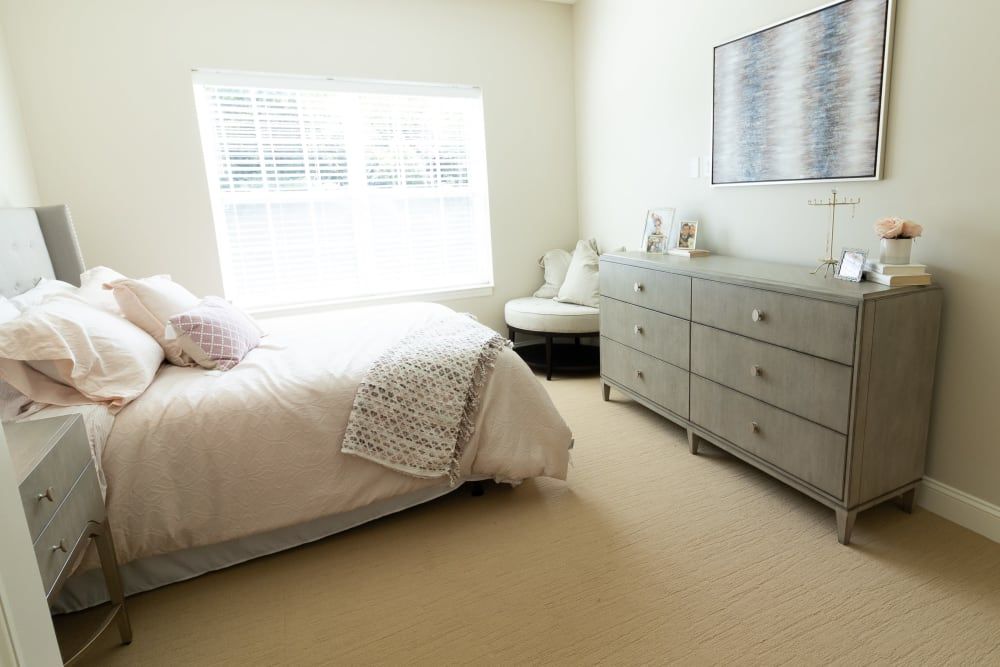 A minimalist bedroom with a double bed, dresser, and a cozy chair by the window.