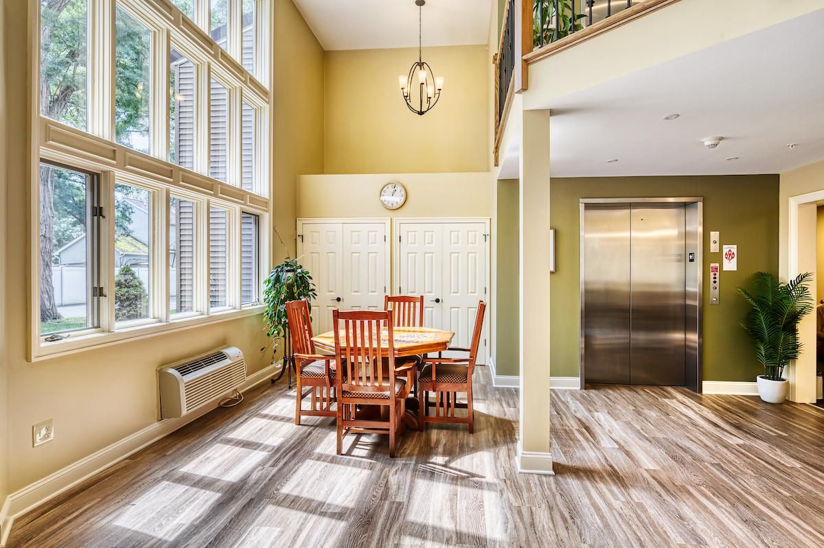 A bright dining area with wooden furniture, large windows, and an elevator, showcasing a modern interior design.