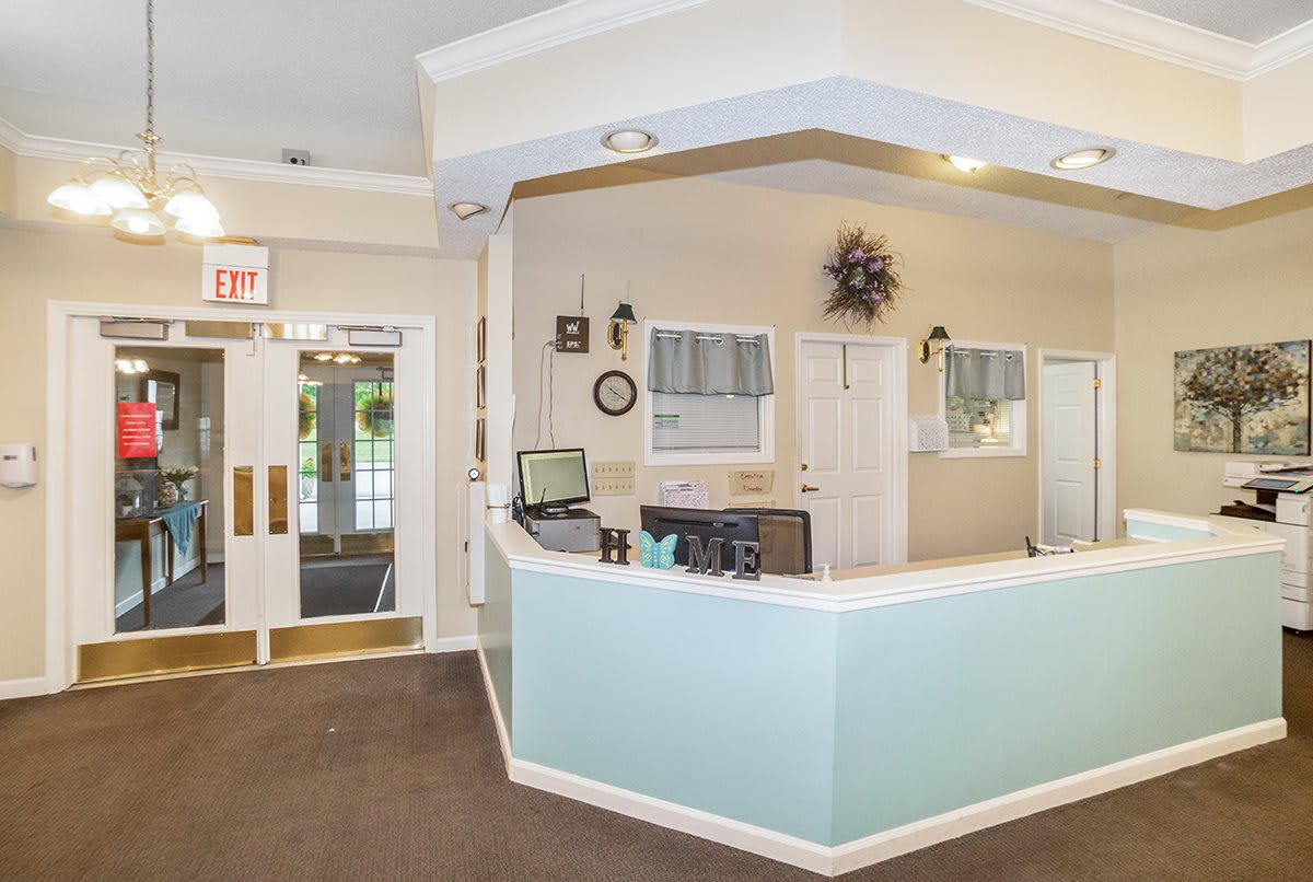 A clean and organized reception area with a desk and computer, decorated with wall hangings and plants.