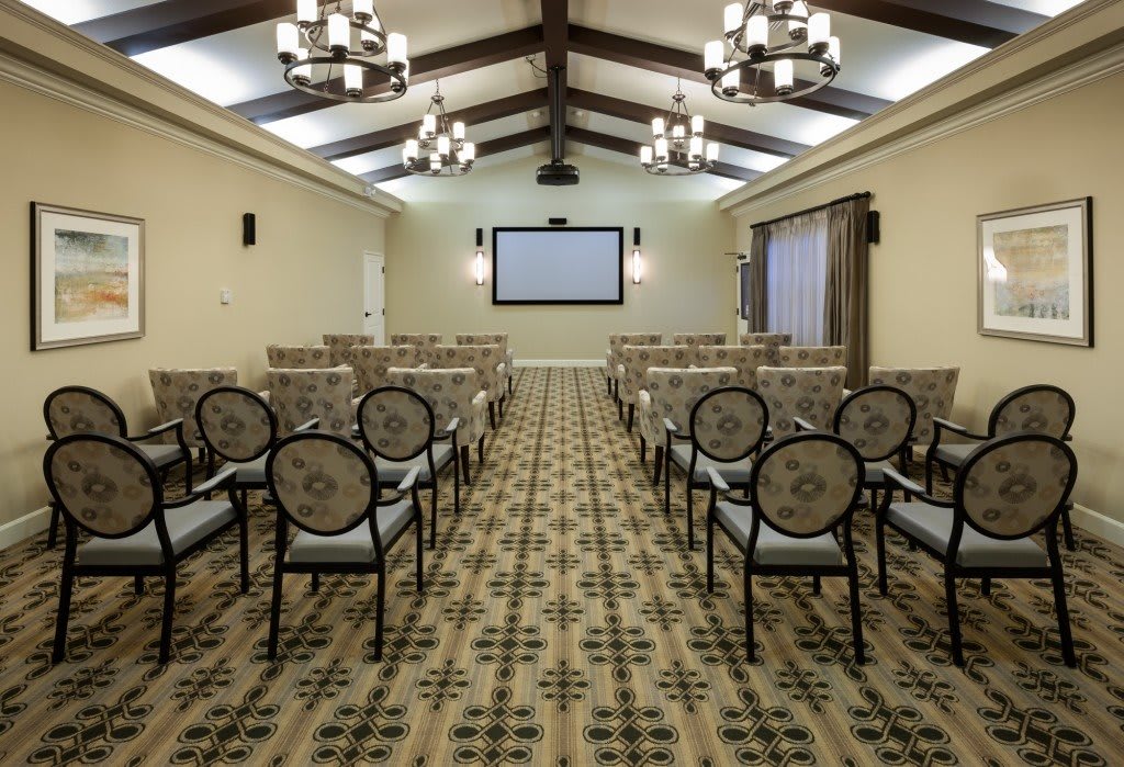 A well-lit conference room equipped with a projector screen and rows of seating, suitable for meetings and presentations.