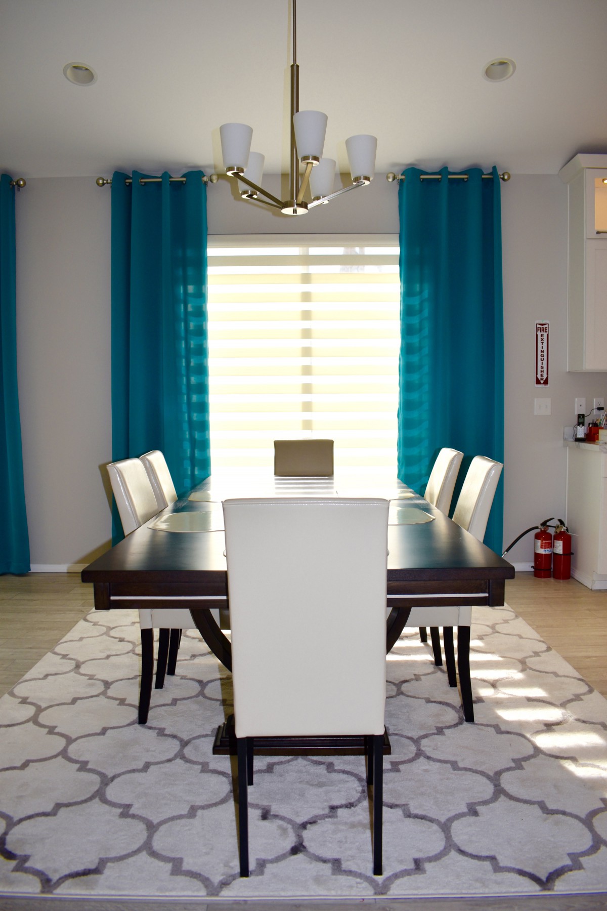 A modern dining room with a dark wooden table, white chairs, and turquoise curtains.