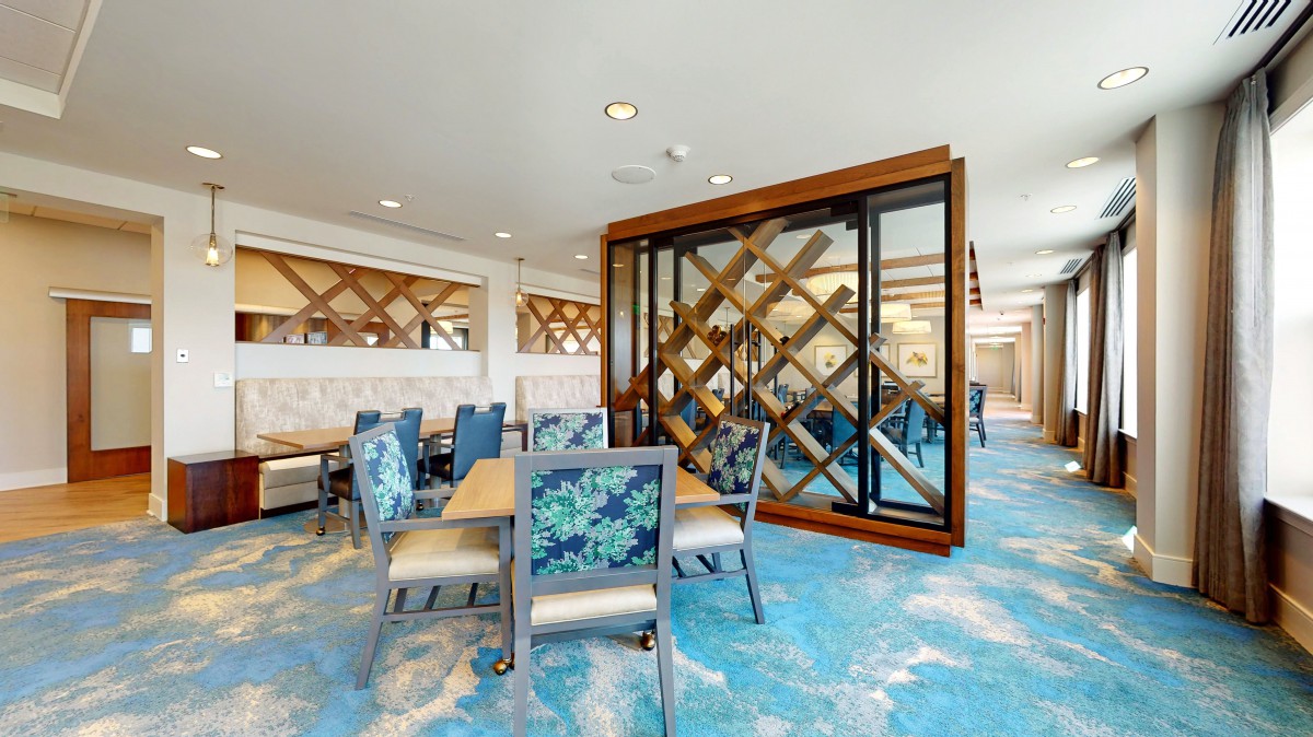 A modern restaurant interior with blue carpeting, wood accents, and tables and chairs arranged for dining.