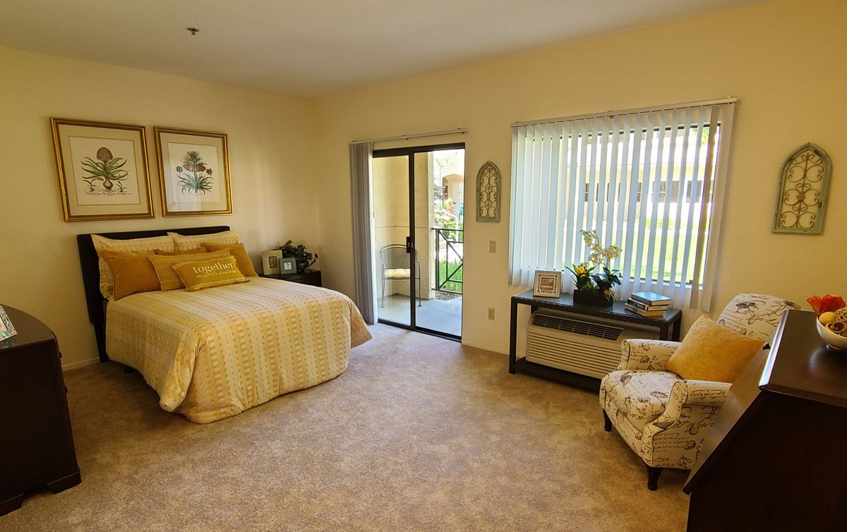 A cozy bedroom with a large bed, comfortable chair, and natural lighting from the window.