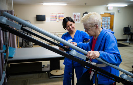 A nurse assists an elderly patient during a physical therapy session, providing support as the patient uses a handrail.